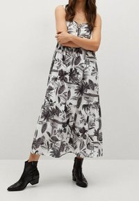 Musta-valkoisella kukkakuviolla varustettu midi-mekko, jossa on nappikiinnitys edessä ja säädettävät olkaimet. Kangas on kevyt.