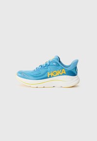 Chaussure de course Hoka en mesh bleu clair avec des accents jaunes. Présente une épaisse semelle intermédiaire blanche et une semelle extérieure texturée pour une meilleure adhérence.