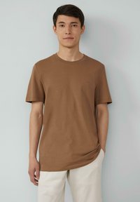 Bruine katoenen t-shirt met korte mouwen en een ronde hals, voorzien van een subtiele logo op de borst. Gecombineerd met lichtgekleurde broeken.