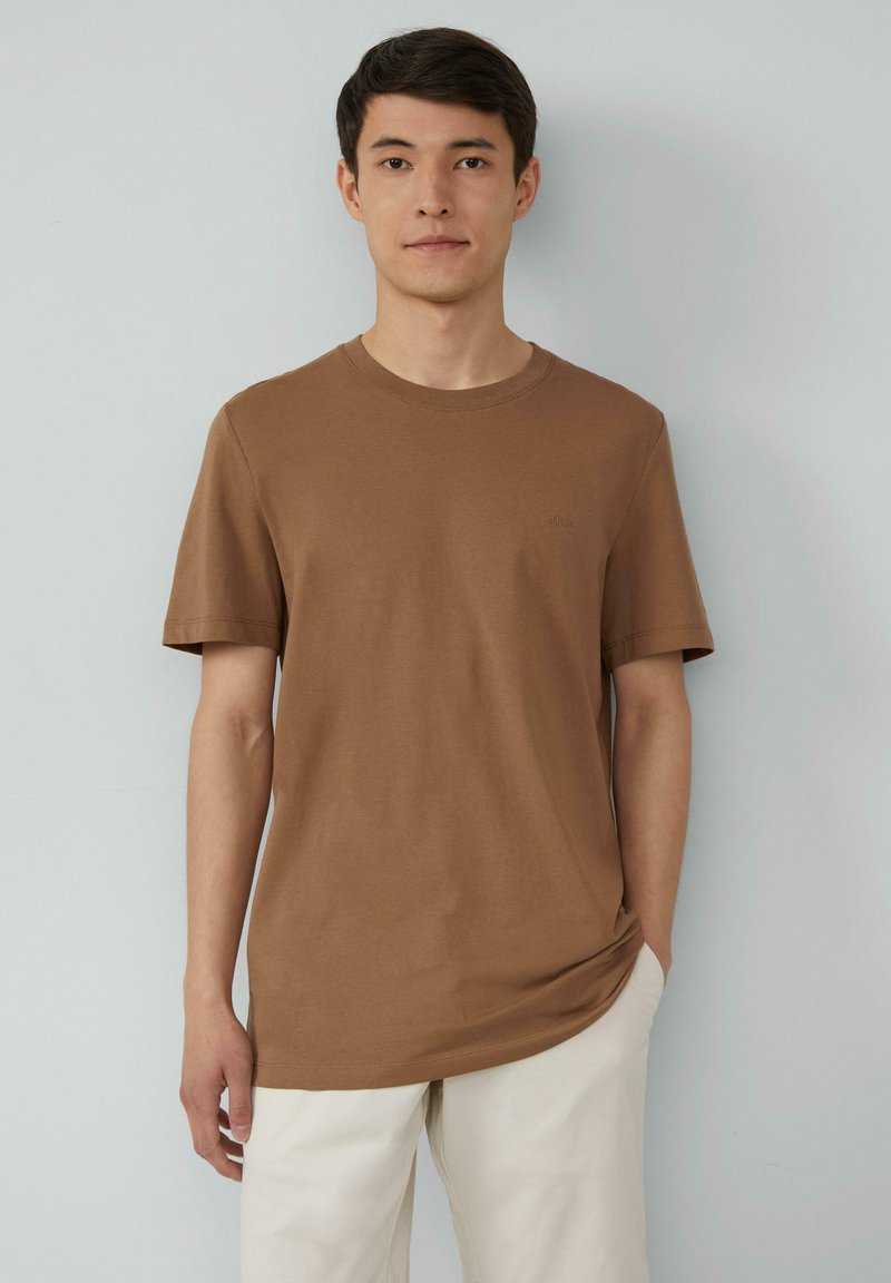 Bruine katoenen t-shirt met korte mouwen en een ronde hals, voorzien van een subtiele logo op de borst. Gecombineerd met lichtgekleurde broeken.