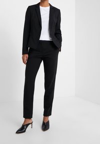 Zwarte op maat gemaakte blazer met een notch lapel, gecombineerd met strakke zwarte broeken en spitse zwarte hakken; gladde stof en een elegant ontwerp.