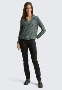Green patterned long-sleeve blouse with a V-neck, paired with black slim-fit pants and black platform shoes. Smooth fabric texture.