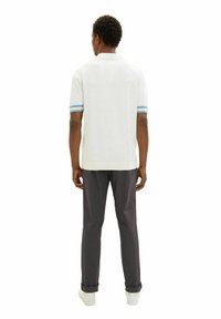 Weißes Polo-Shirt mit blau gestreiften Manschetten, kombiniert mit dunkelgrauen Hosen. Das Design ist schlicht, mit einem klassischen Kragen und einem geraden Schnitt.