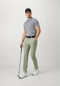 Γκρι πόλο μπλούζα, ανοιχτοπράσινα παντελόνια, μαύρη ζώνη, λευκά αθλητικά παπούτσια. Κρατώντας μια γκολφ κλάμπ, φοράει ένα σκούρο καπέλο. Απλός, μοντέρνος σχεδιασμός.