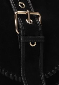 Zwarte suède tas met een glanzende gouden gesp, voorzien van een gestikte leren schouderband en metalen oogdetails aan de zijkant.