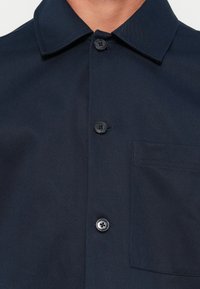 Close-up of a navy blue button-up shirt with a chest pocket and a collar, worn by a person.