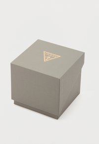 Grijs rechthoekig cadeauverpakking met een getextureerd oppervlak en een gouden driehoeklogo bovenop. De doos heeft een deksel en een strak, eenvoudig ontwerp.