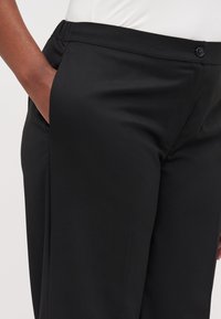 Black trousers made of smooth fabric, featuring a classic design with a button closure, side pockets, and a tailored fit.