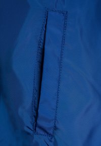 Niebieska tkanina nylonowa o gładkiej powierzchni, z pionową kieszenią szczelinową i starannym wykończeniem krawędzi.