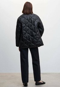 Czarna pikowana kurtka o pudełkowym kroju, z okrągłymi wzorami, długimi rękawami i gładką, błyszczącą teksturą, w połączeniu z ciemnymi spodniami i balerinami.