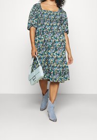 Kukallinen, polvipituinen mekko puffihihnoilla, neliökaula-aukolla, siniharmaat mokkanahkasaappaat ja vaaleansininen käsilaukku.