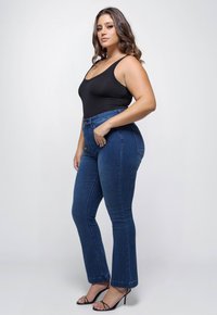 Zwarte tanktop, hoge taille blauwe spijkerflared jeans, gladde textuur, slim fit, en zwarte open teen hakken. Eenvoudig ontwerp, geen zichtbare patronen.