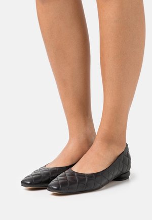 Ballerines en cuir noir avec un design matelassé, bout rond et petit talon. Texture lisse et style minimaliste.