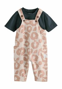 Salopette à imprimé léopard tan avec grandes poches, bretelles ajustables et boutons marron, assortie à un t-shirt vert foncé. Tissu en mélange de coton.