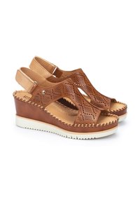 Sandales compensées en cuir marron avec des découpages, bride arrière réglable et semelle en caoutchouc blanche. Détails surpiqués le long des bords.