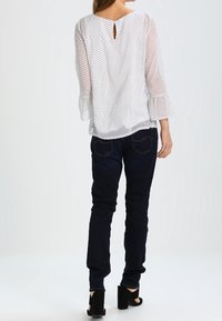 Blusa bianca a pois con maniche trasparenti e dettaglio a chiave sul retro. Abbinata a jeans blu scuri a fascia e scarpe nere con tacco a blocco.