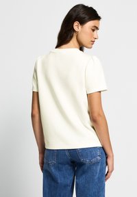 Haut court jaune pâle à manches courtes avec un col rond et des manches légèrement bouffantes ; associé à un jean en denim bleu clair. Texture lisse.