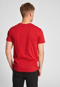 Rød kortærmet t-shirt lavet af letvægtsbomuld, med en rund halsudskæring og en glat overflade, set fra ryggen.