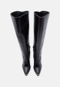 Ψηλές μαύρες δερμάτινες μπότες με μυτερές μύτες και διακριτική διακοσμητική ραφή, ορατές από πάνω σε λευκό φόντο.
