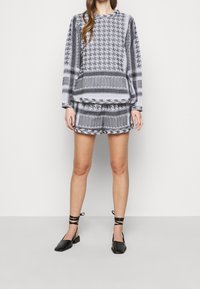 Šedá a černá vzorovaná mikina s odpovídajícími šortkami a černými botami na blokovém podpatku. Materiál má geometrické vzory a volný střih.