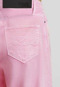 Růžové denimové kalhoty se zadní kapsou vyšitým nápisem "Karl" a černou koženou nášivkou s označením "Karl Lagerfeld" na pásku.