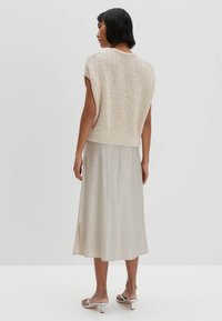 Top corto in maglia beige a maniche corte con un motivo testurizzato, abbinato a una lunga gonna di lino grigia chiara con uno spacco laterale e sandali semplici.