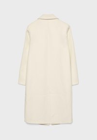 Cappotto lungo color crema realizzato in tessuto liscio, con collo a rever, maniche lunghe e spacco centrale sul retro. Assenza di accessori visibili.