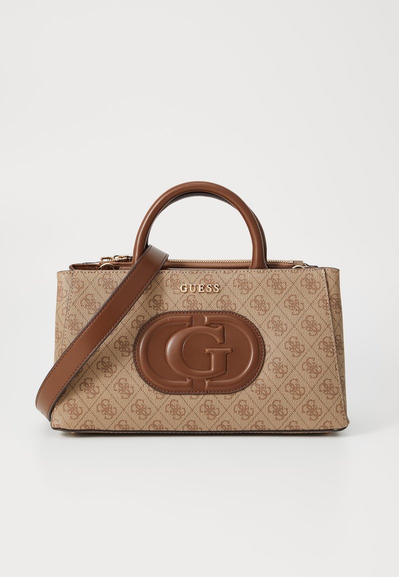 Sac à main Guess beige et marron avec motif logo intégral, grand emblème "G" embossé, poignées supérieures et bandoulière amovible sur fond blanc.