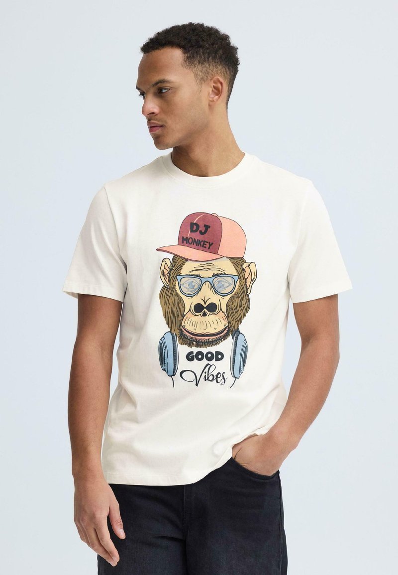 Jeune homme portant un t-shirt blanc avec un dessin d'un singe DJ portant un chapeau, des lunettes, un casque audio et le texte "Good Vibes".