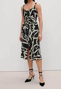 Robe à motif noir et crème avec un corsage ajusté, des bretelles réglables, des boutons sur le devant et une jupe fluide à hauteur des genoux.