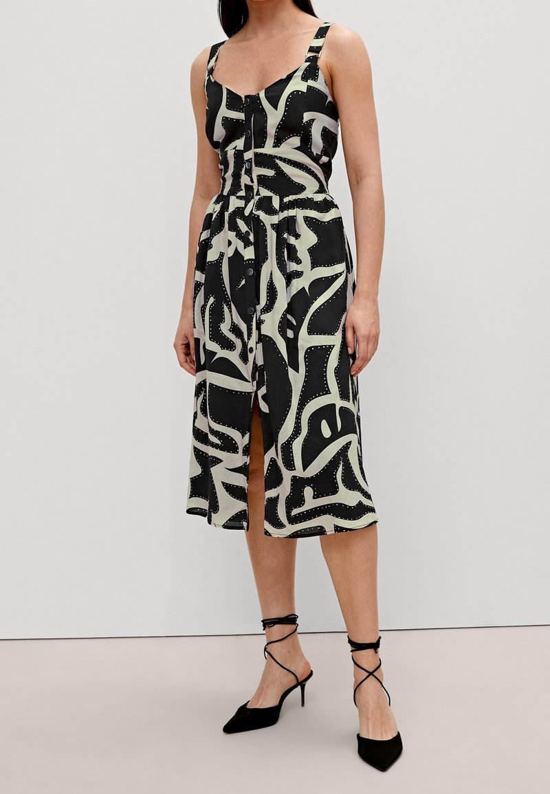 Robe à motif noir et crème avec un corsage ajusté, des bretelles réglables, des boutons sur le devant et une jupe fluide à hauteur des genoux.