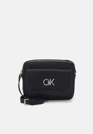 Sac bandoulière rectangulaire noir avec sangle réglable, poche avant à rabat et logo argenté "CK" sur tissu à motif avec initiales "CK" répétées.