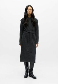 Abito lavorato a maglia lungo di un grigio scuro, con una vita cinturata, spalle a costine e maniche lunghe, abbinato a stivali neri fino al ginocchio.