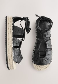 Sorte læderespadrilles med flettet jutesål, der har en tekstureret finish og justerbare ankelstropper for en sikker pasform.