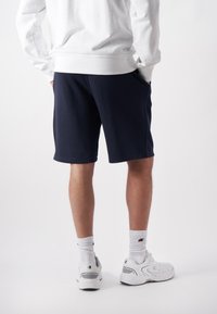 Dark navy athletic shorts with side pockets, made of soft fabric. Worn with a white sweatshirt and white sneakers with gray accents.