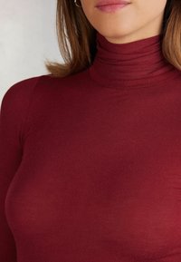 Burgundy polokrage topp med en figursydd design, som har mjukt, stretchigt tyg och subtila ruggade detaljer runt kragen.