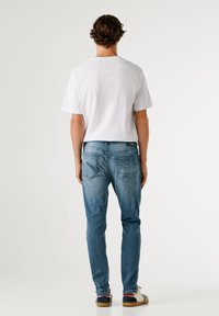 Camiseta de algodón blanca de manga corta, vaqueros de denim azul claro con un patrón de la Union Jack en el bolsillo trasero y zapatillas azules con suelas blancas.