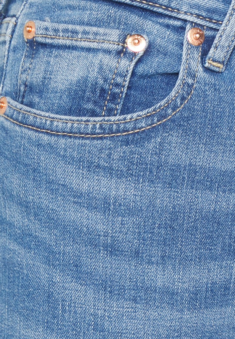 Tissu en denim bleu clair avec une légère texture délavée, comportant des rivets en cuivre et un petit détail de poche avant.