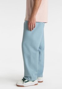 Light blue cotton trousers with a relaxed fit, featuring a smooth texture and side pockets, paired with white sneakers and green accents.