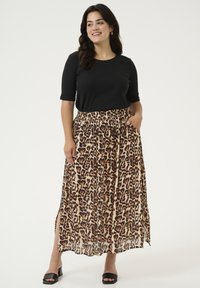 Haut noir à manches courtes avec une jupe maxi à imprimé léopard marron, dotée d'une taille élastique et de poches latérales ; portée avec des sandales à talons blocs noires.