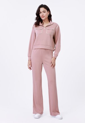 Roze tweedelige lounge-set met een ritsloze pullover met twee borstzakken en bijpassende wijd uitlopende broeken. Glad, rekbaar materiaal.
