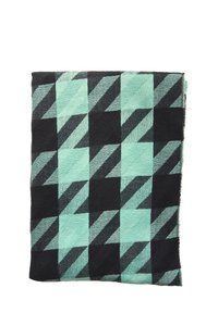 Manta tejida en azul verdoso y negro con un patrón geométrico que presenta formas en zigzag y cuadrados. Superficie texturizada con bordes con flecos.