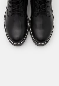 Bottes en cuir noir avec une finition lisse, bout rond, et une couture blanche contrastante le long de la semelle. Dotées de lacets pour un ajustement sécurisé.