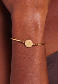 Gouden armband met een ronde, met een hart gegraveerde bedel en een kleine steenaccent, met een gladde, reflecterende afwerking op een slanke band.