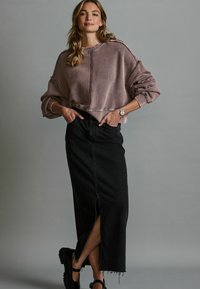 Felpa viola oversize con cuciture visibili, abbinata a una lunga gonna di jeans nera con uno spacco laterale e scarpe platform nere.