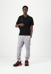 Black short-sleeve shirt, light gray joggers with elastic cuffs, and black/red sneakers. Minimalist design with distinct colors and textures.