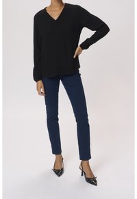 Haut noir à manches longues avec un col en V, en tissu texturé, et coupe décontractée, associé à un pantalon slim bleu foncé et des escarpins noirs pointus.