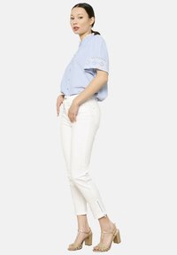 Lichtblauw overhemd met kantaccenten, gecombineerd met witte slim-fit broeken en gouden haksandalen, met ritsdetails bij de enkels.