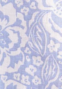 Tissu bleu et blanc avec un motif floral comprenant de grandes fleurs, des feuilles et de petits boutons dans une texture tissée.