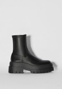 Botte en cuir noire mi-mollet avec semelle épaisse et robuste et bout arrondi, photographiée de profil sur un fond clair uni.